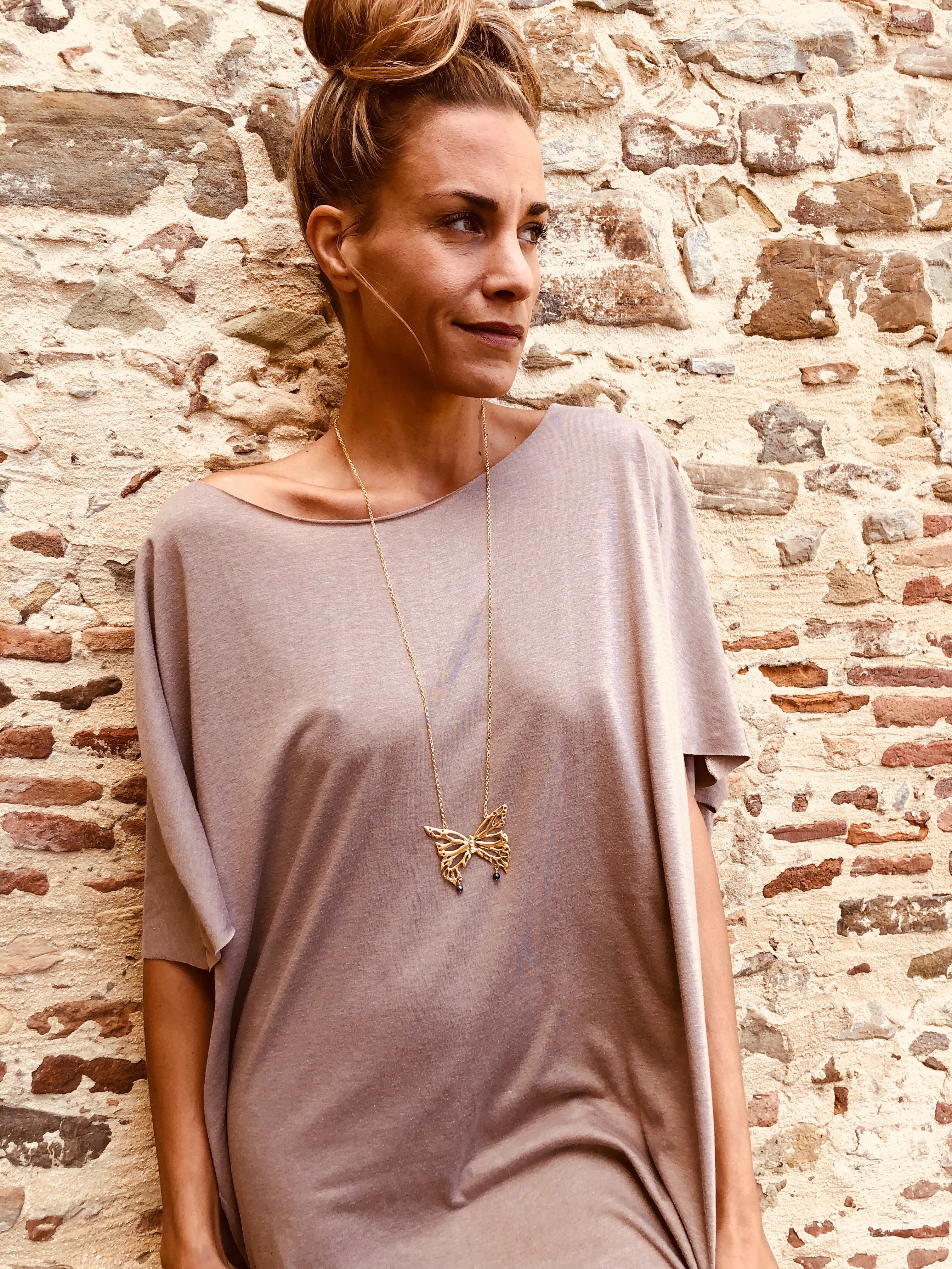 Model leaning on a wall wearing a long goldplated Butterfly Necklace - Charms Collection - Jennifer Kinnear Jewellery