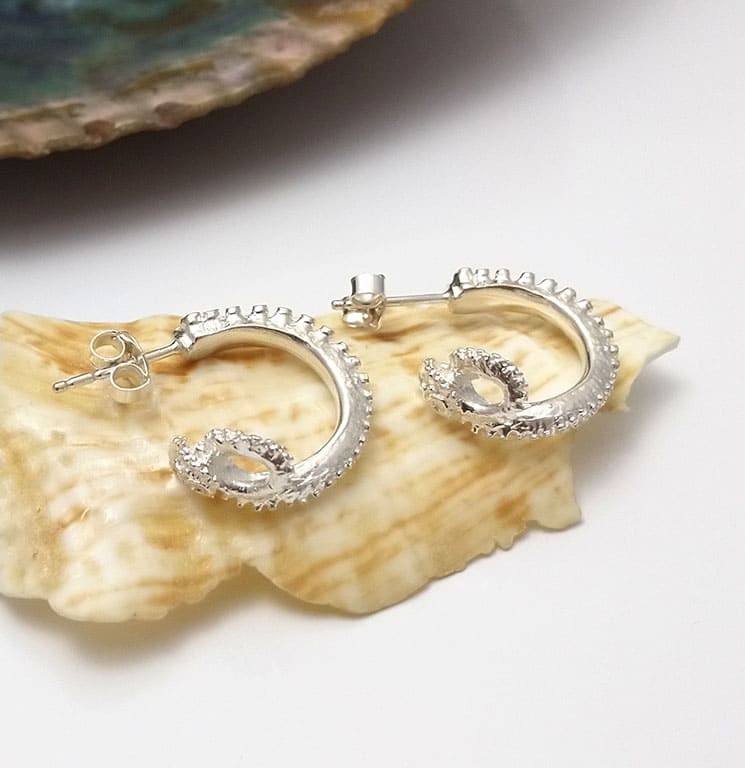 Handmade silver octopus hoop earrings displayed on a seashell, by Jennifer Kinnear.