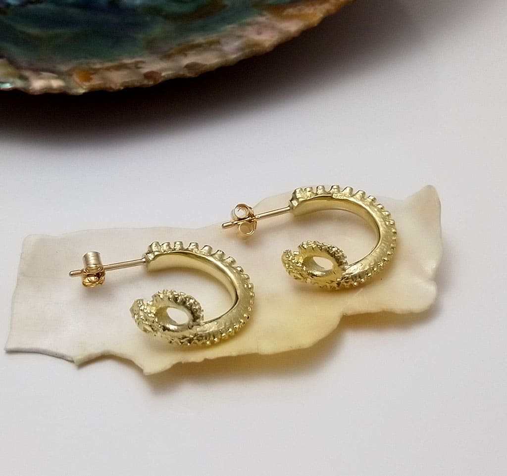 Handmade gold octopus earrings, displayed on a seashell, by Jennifer Kinnear.